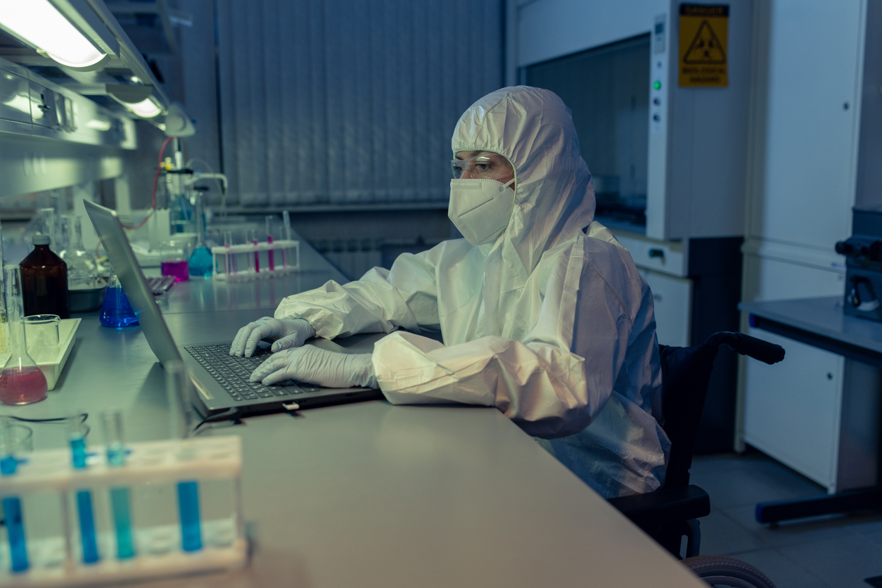 Female scientist in protective workwear sitting at the table and typing on laptop during her work in the lab