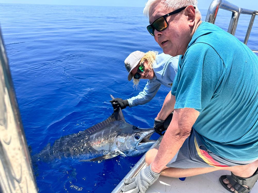 Mr GK Goh perched on the side of a boat in the ocean off Western Australia with a blue marlin