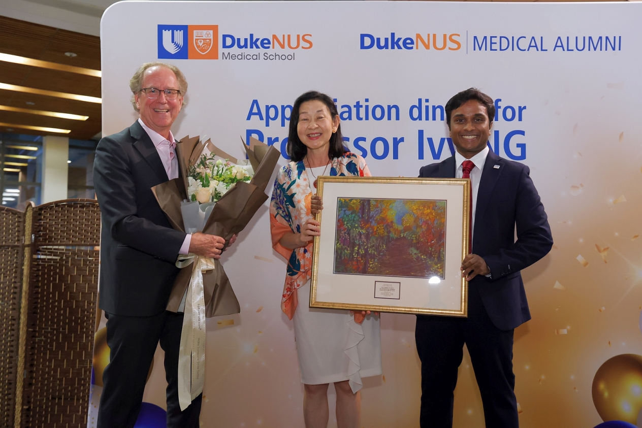 Dean Coffman (left) presents Prof Ng (centre) with a token of appreciation from Duke-NUS Governing Board Chairman Mr Goh Yew Lin. They are joined by Dr Shashendra Aponso on stage (right) with his painting to Prof Ng titled “The forest is gold”.