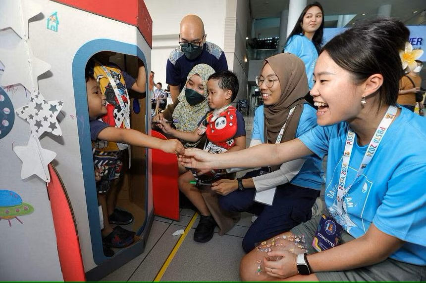 Photo of a young child inside a cardboard rocket with camp organisers playing with him